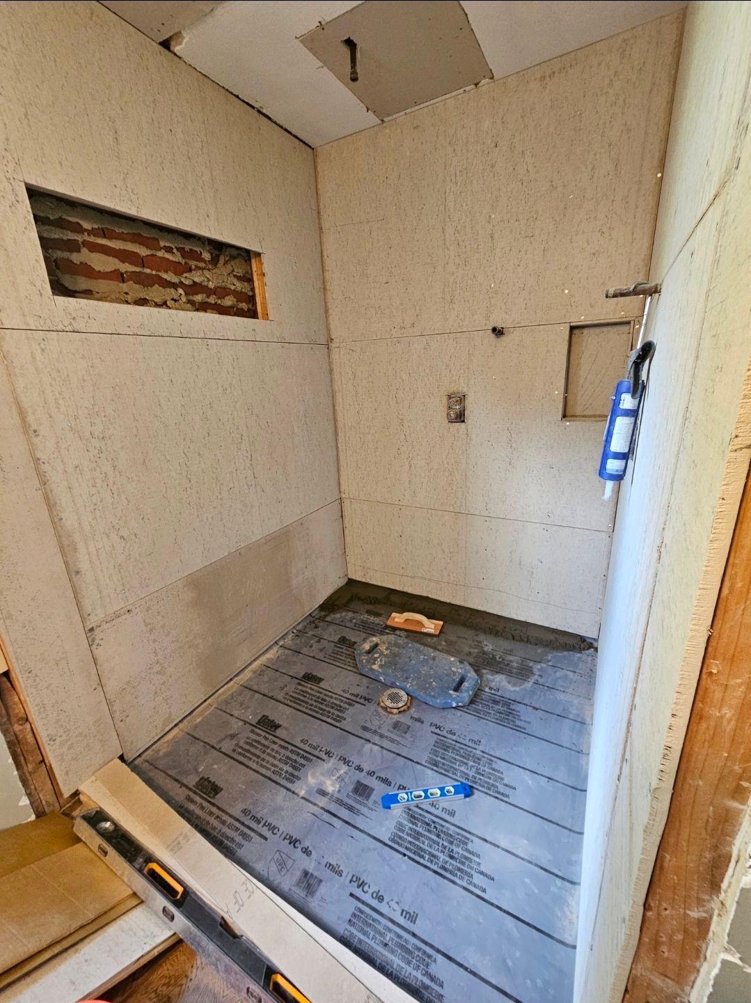 A shower under construction with cement board walls, a membrane-covered floor, and visible plumbing.