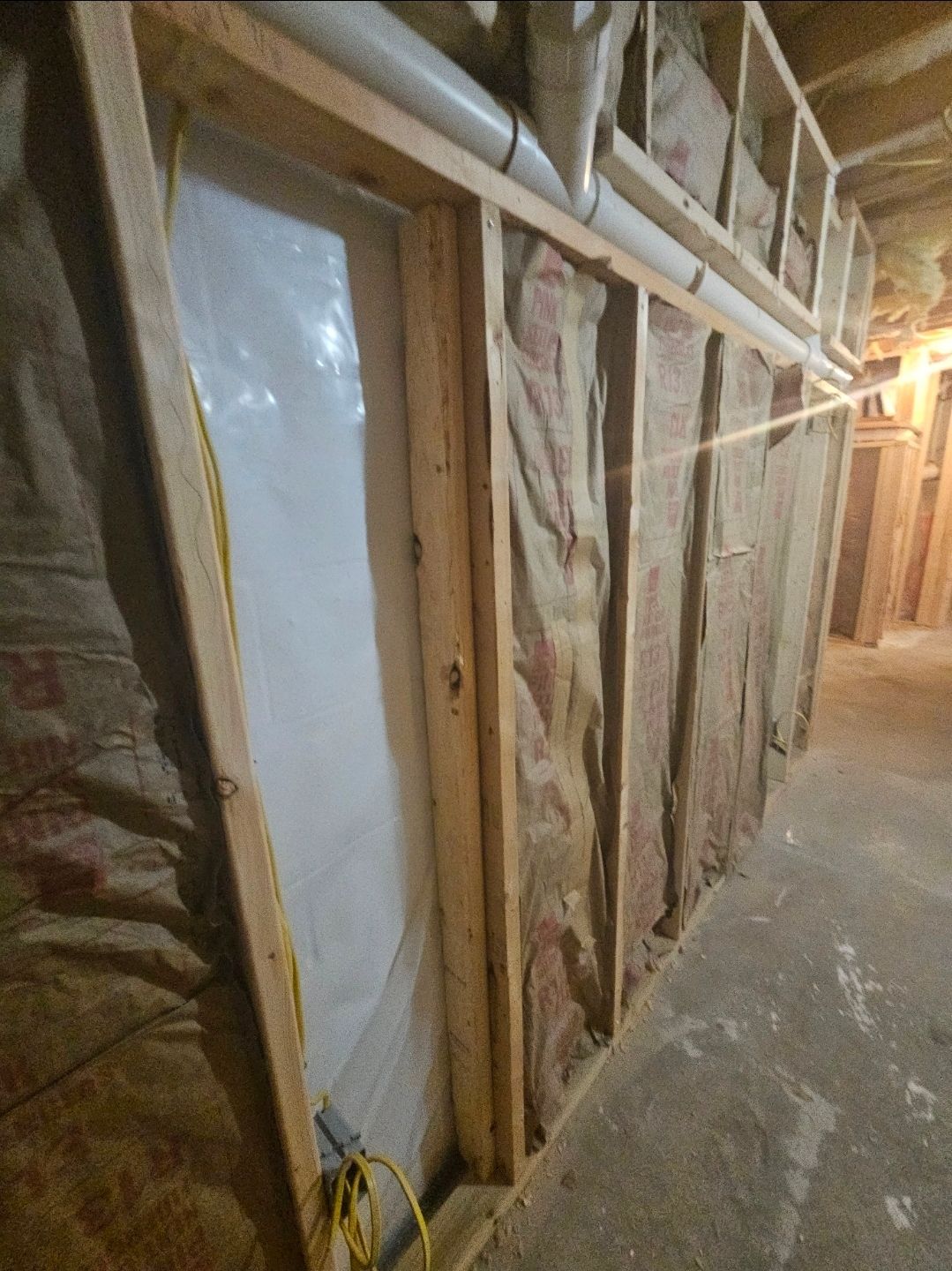 Framed wall with insulation and plastic sheeting. Basement setting, with concrete floor and exposed wood beams.