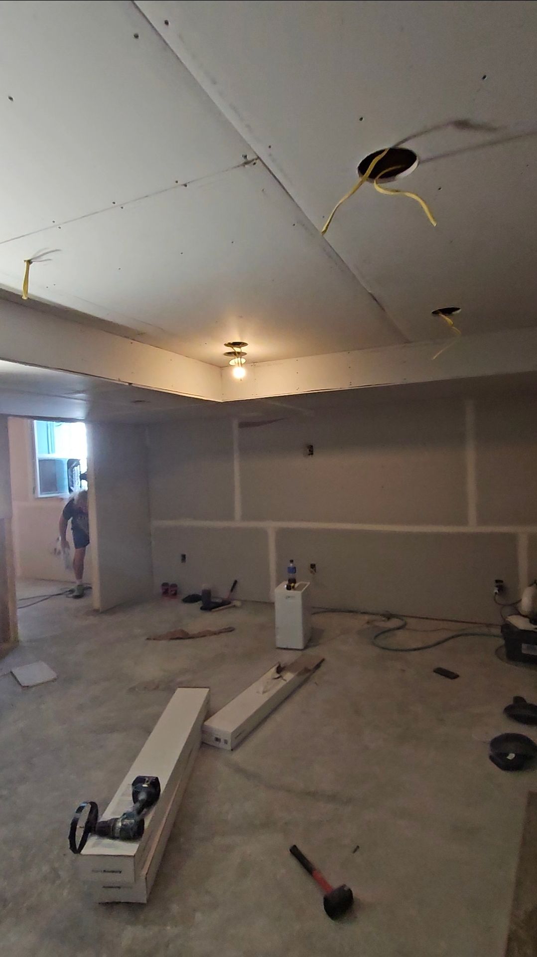 Basement under renovation with exposed drywall, electrical wiring, and a person in the background.