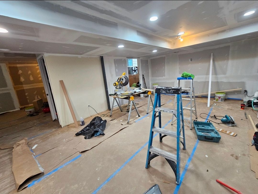Room under construction; drywall, tools, and ladders scattered on wood floor.