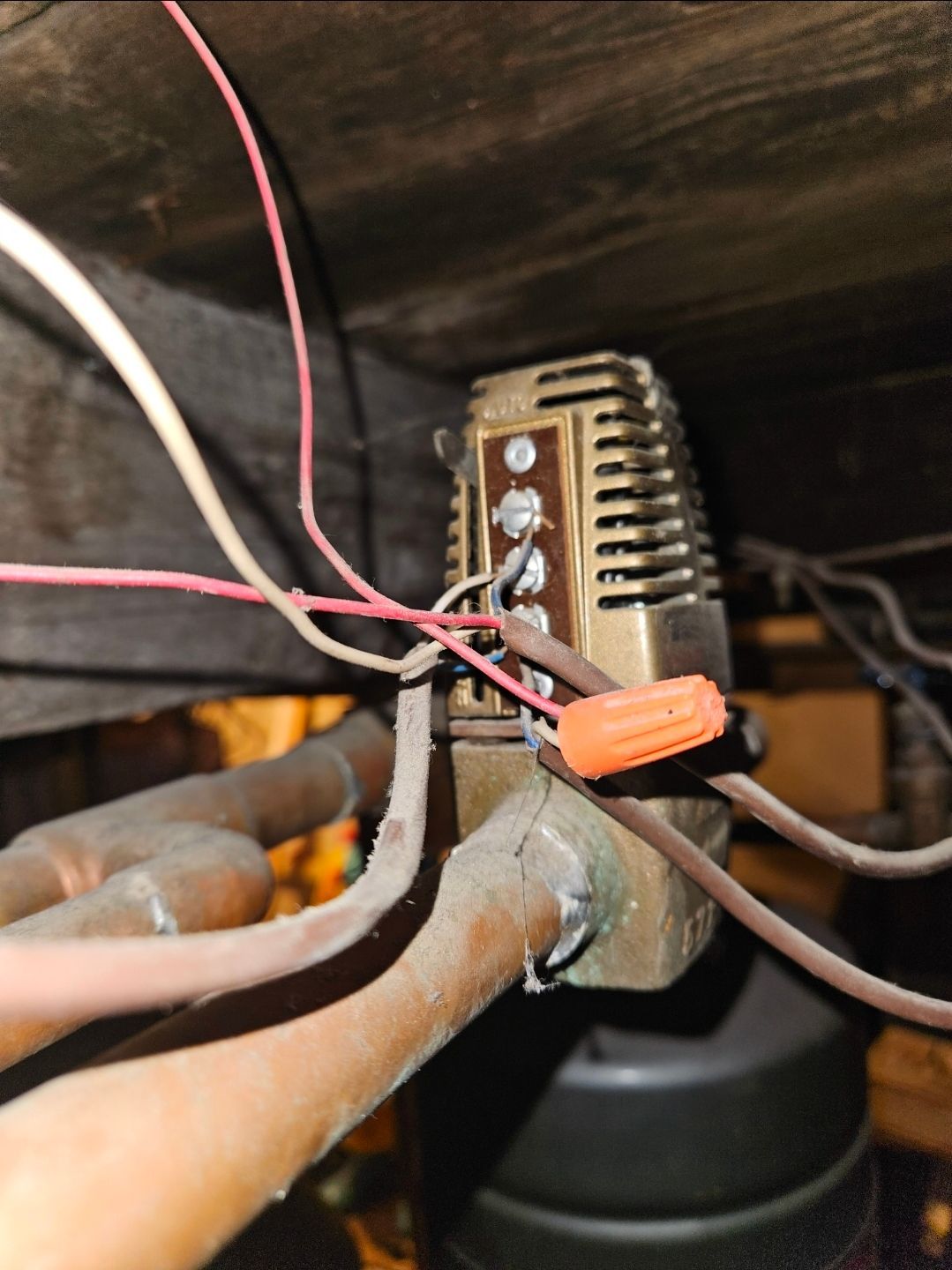 Copper pipes and electrical wires connected to a brass-colored thermostat within a dark enclosure.