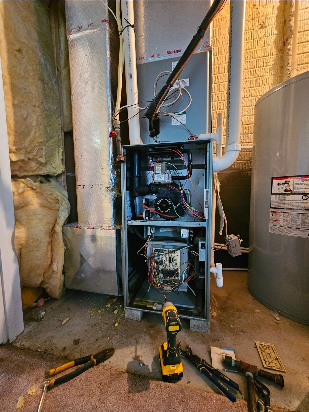 Furnace repair: open furnace cabinet, tools on the floor. Interior setting, exposed wires, and ductwork visible.