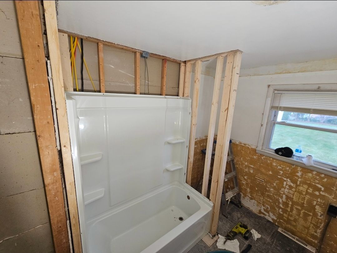 A partially constructed bathroom with a white tub and shower surround. Framing and exposed wires are visible.