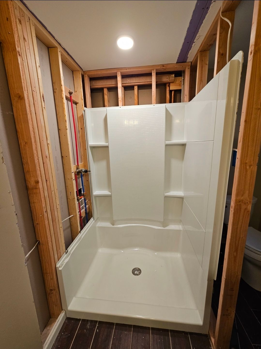 White shower stall installed in a framed-out bathroom during renovation.