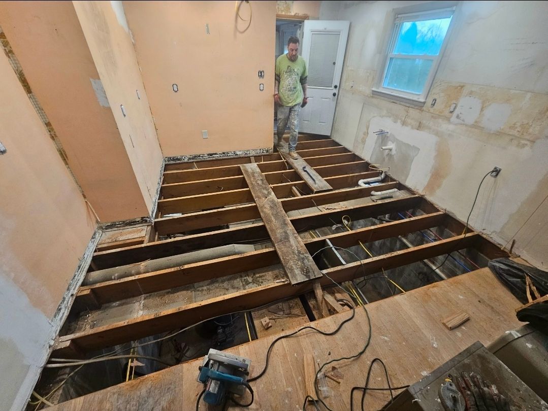 Room under renovation, floorboards removed exposing joists; person standing in the room.