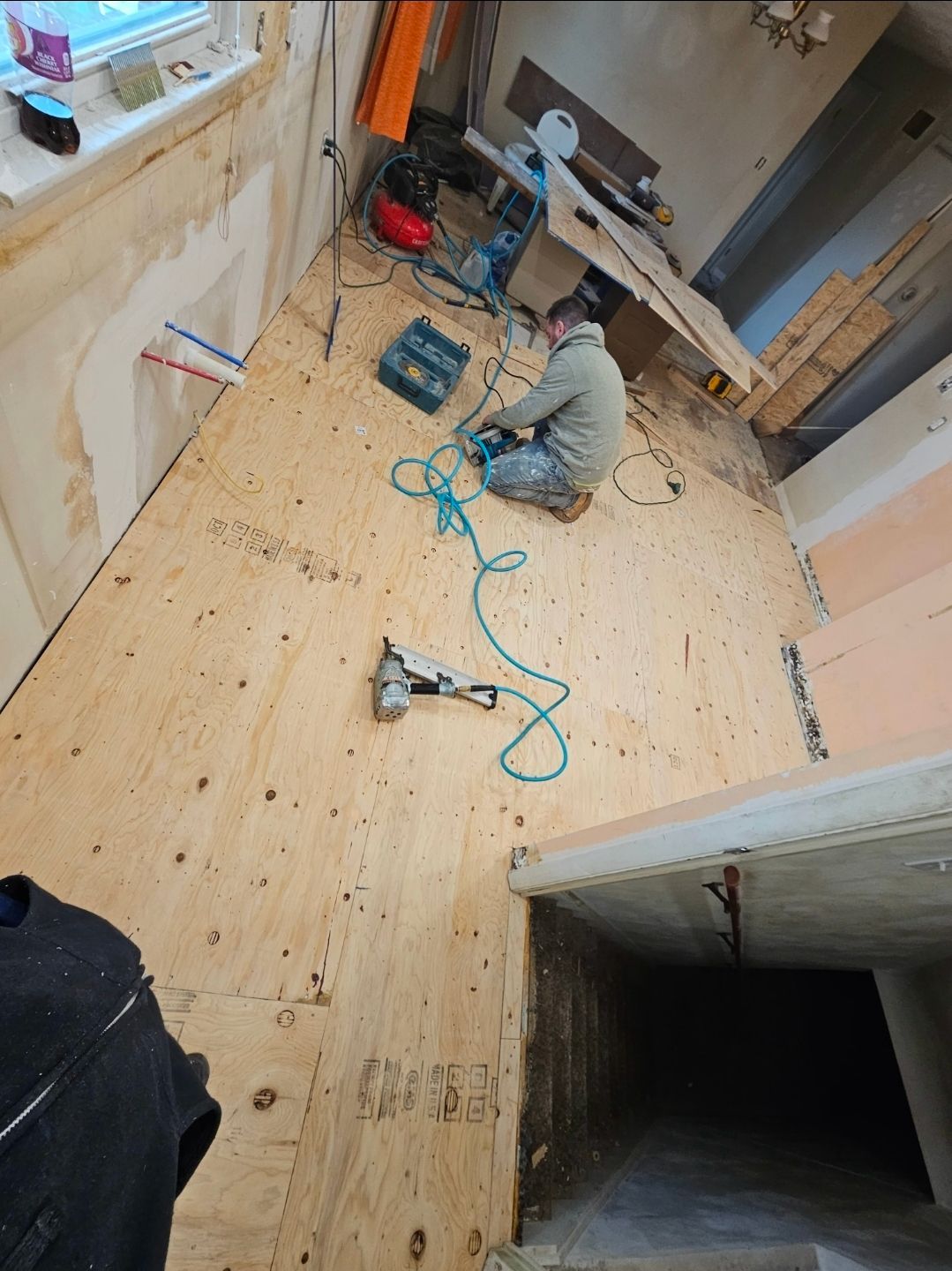 Person installing wooden flooring in a room under renovation, with tools scattered around.