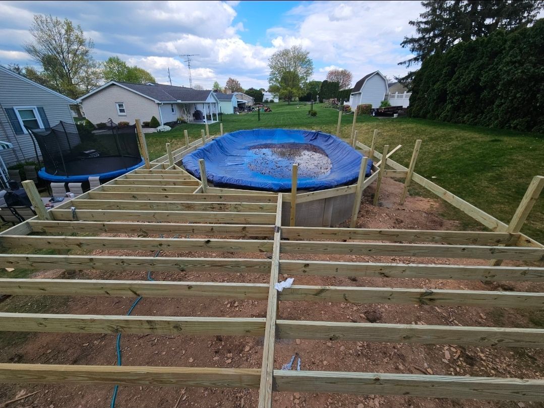 A backyard with a partially built wooden deck around a covered above-ground pool.