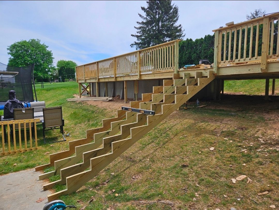 Wooden deck with stairs leading down to the ground. Construction is ongoing.