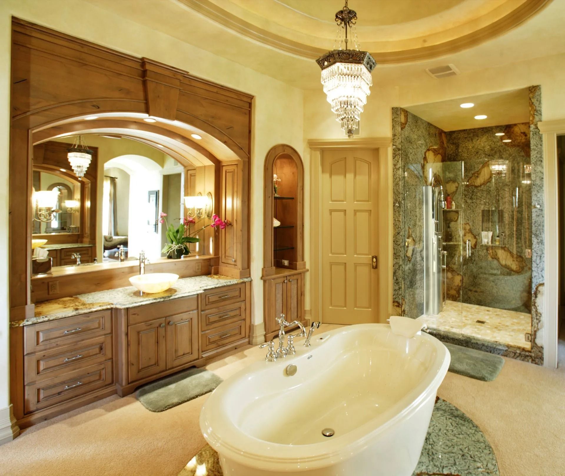 Luxurious bathroom with soaking tub, glass shower, wood cabinetry, and crystal chandelier.