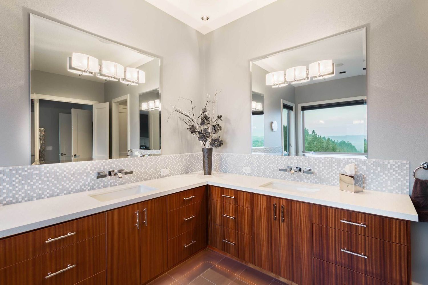 Modern bathroom with wooden cabinets, white countertops, two large mirrors, and decorative vase.