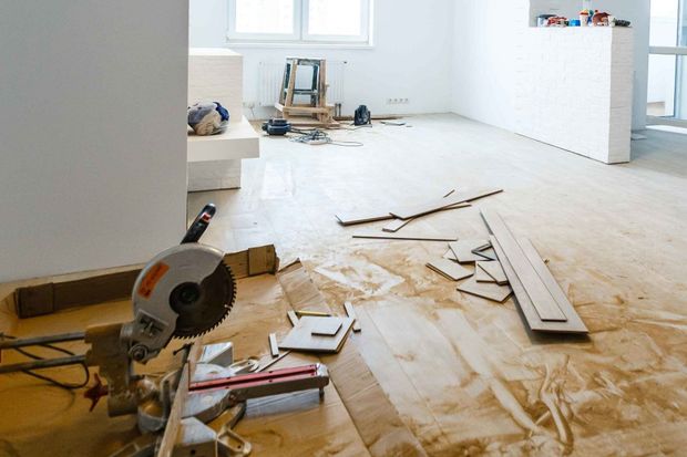 Miter saw on floor with wood pieces, debris, and tools in a room under construction.