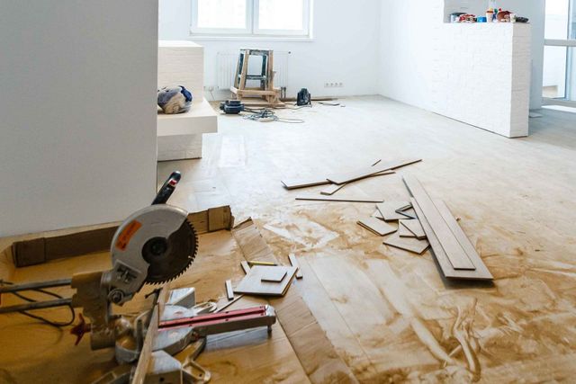 Miter saw on floor with wood pieces, debris, and tools in a room under construction.