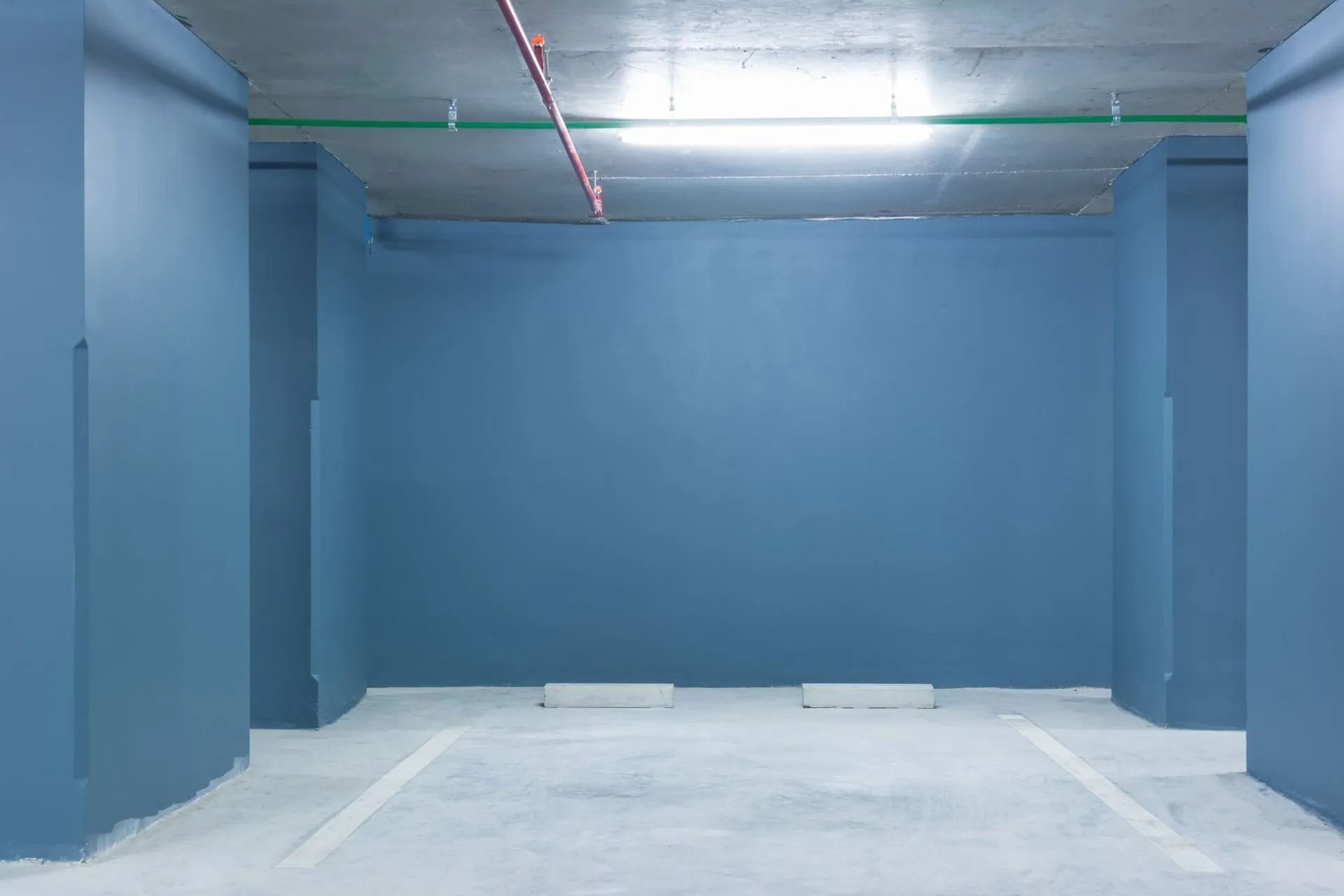 Empty blue parking spot in a parking garage with painted walls and ceiling, white parking lines.