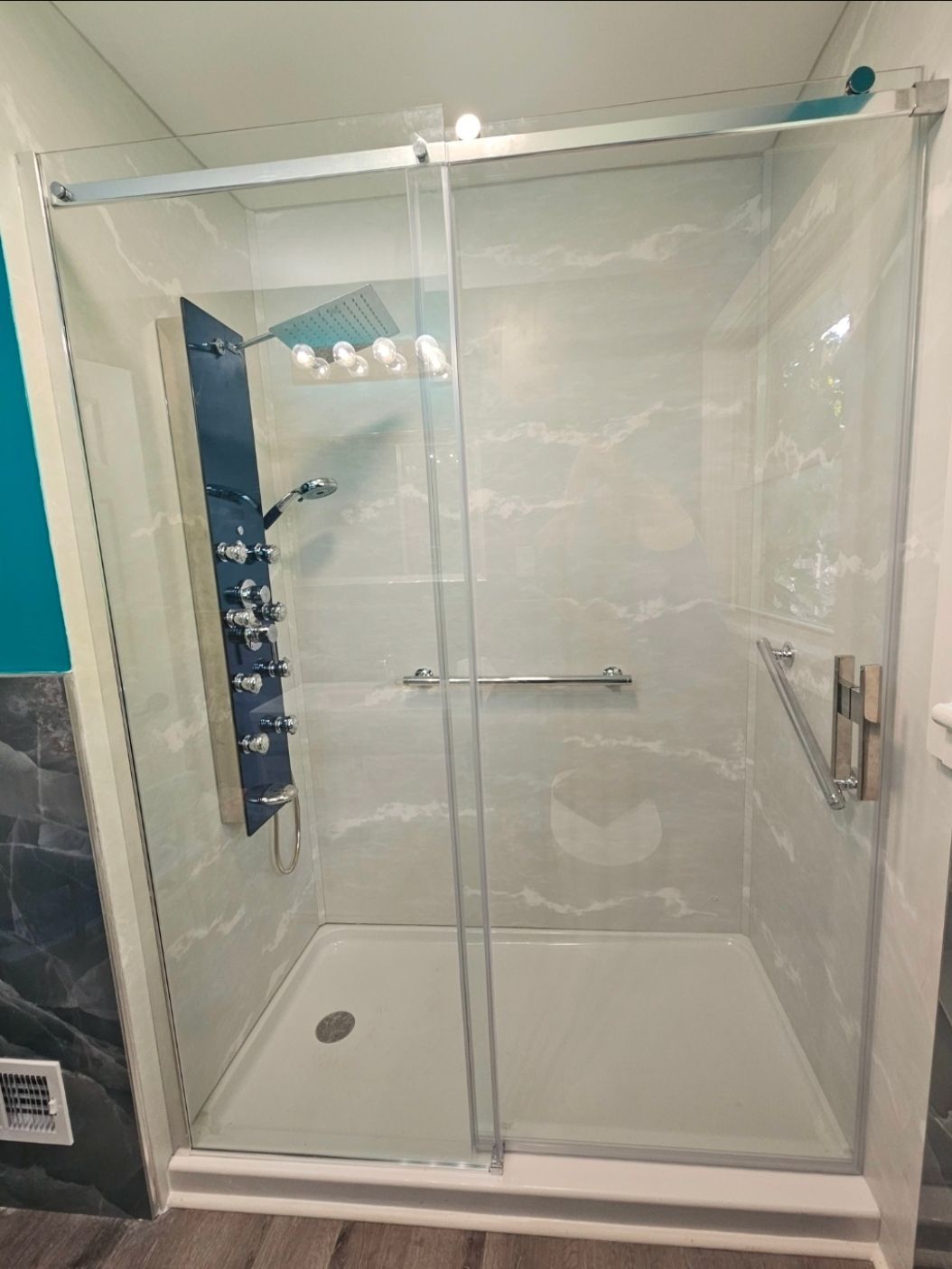 Accessible shower with sliding glass doors, grab bars, and a multi-head shower fixture.