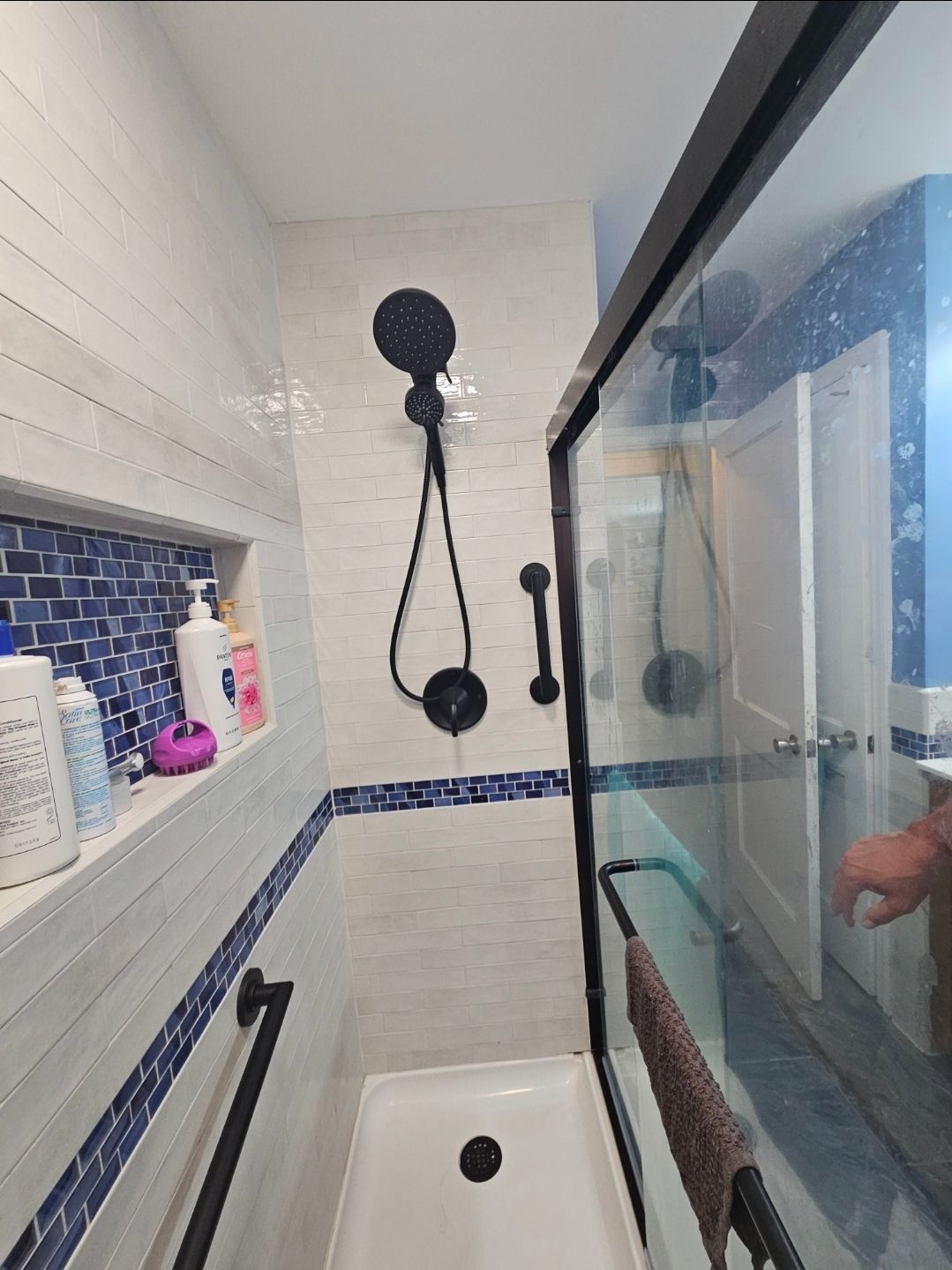 Small, tiled shower with glass door, black fixtures, and built-in shelf.