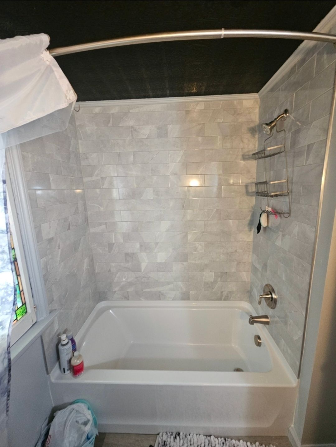 White bathtub and shower with gray tiled walls, stainless steel fixtures, and a curved shower rod.