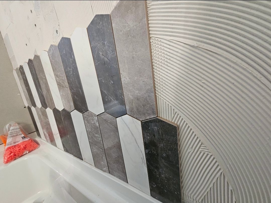Tiling in progress: Gray, white, and black elongated hexagon tiles on a wall with applied mortar.