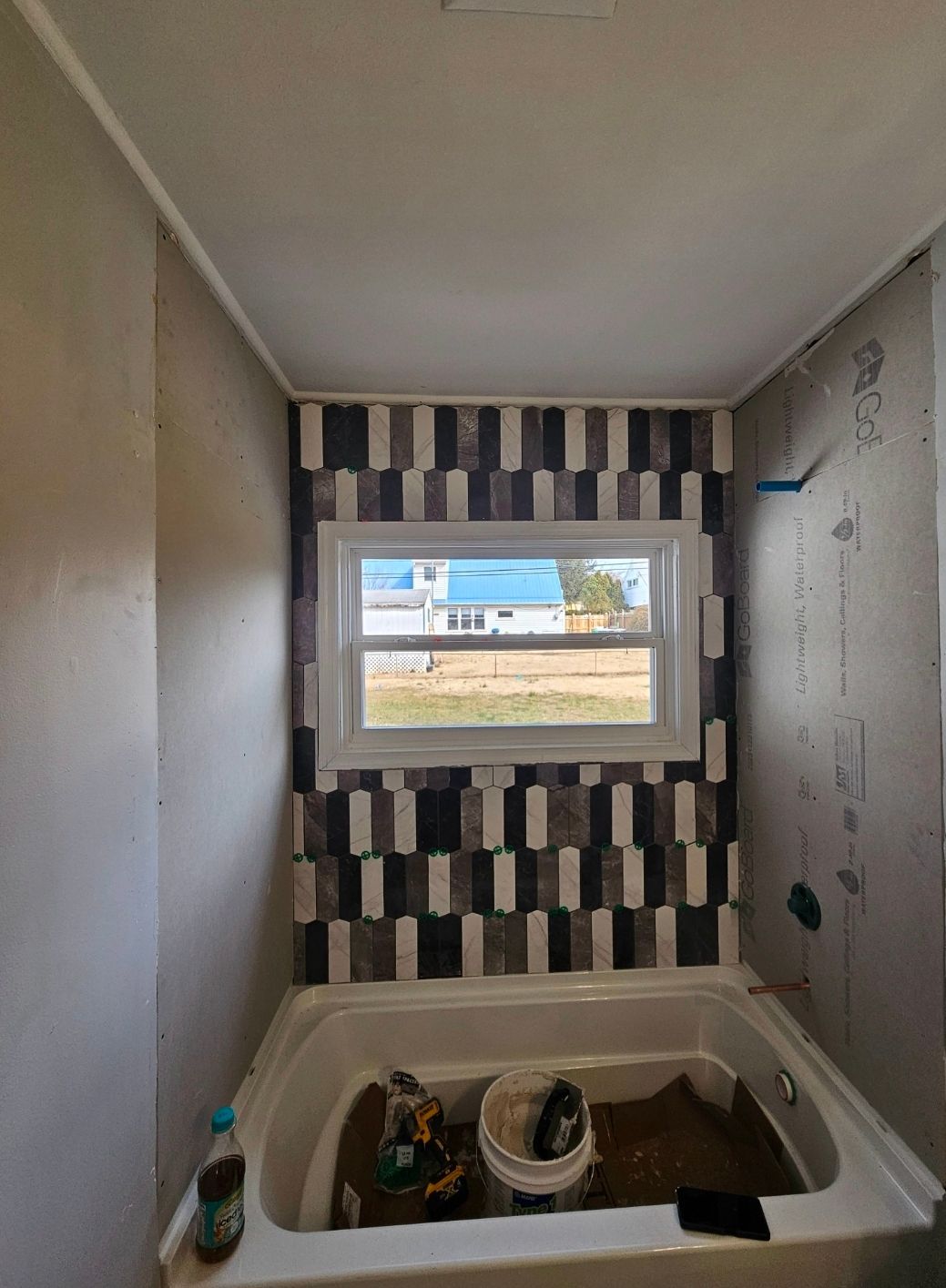 Bathroom with patterned tile backsplash, a window, and a white bathtub.