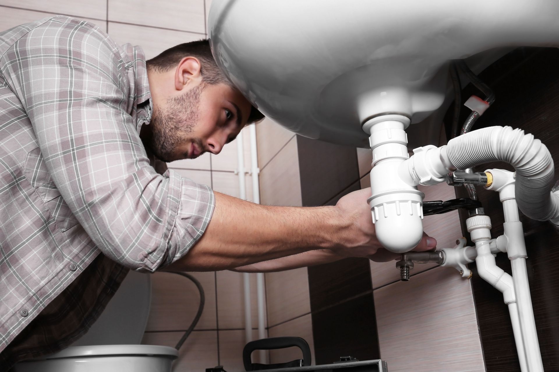 Plumber working under a white bathroom sink, using tools.