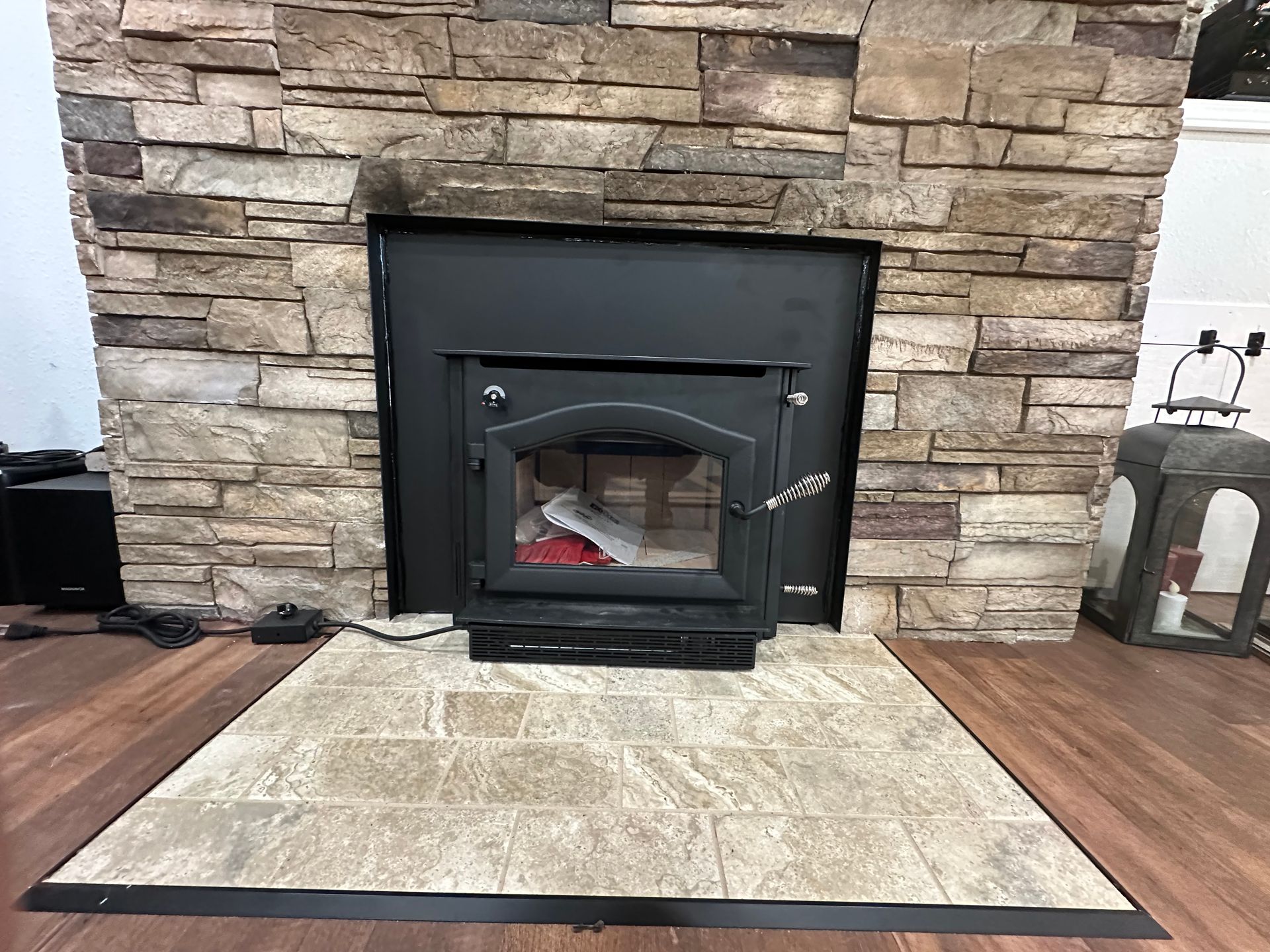 Fireplace with a stone facade, black stove insert, and tile hearth.