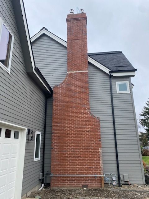 Red brick chimney on the side of a gray house with a black roof.