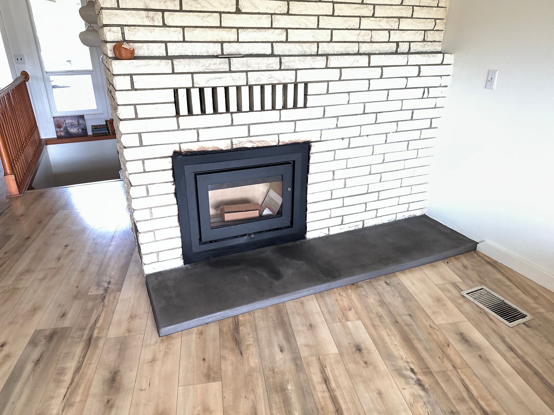 Brick fireplace with a dark metal firebox and gray hearth in a room with wood-look flooring.
