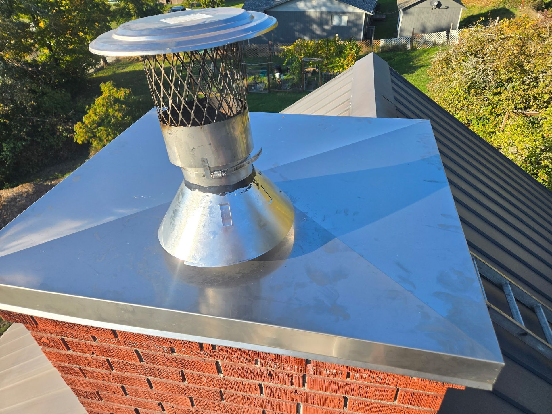 Metal chimney cap on a brick chimney with a metal roof, captured from above.