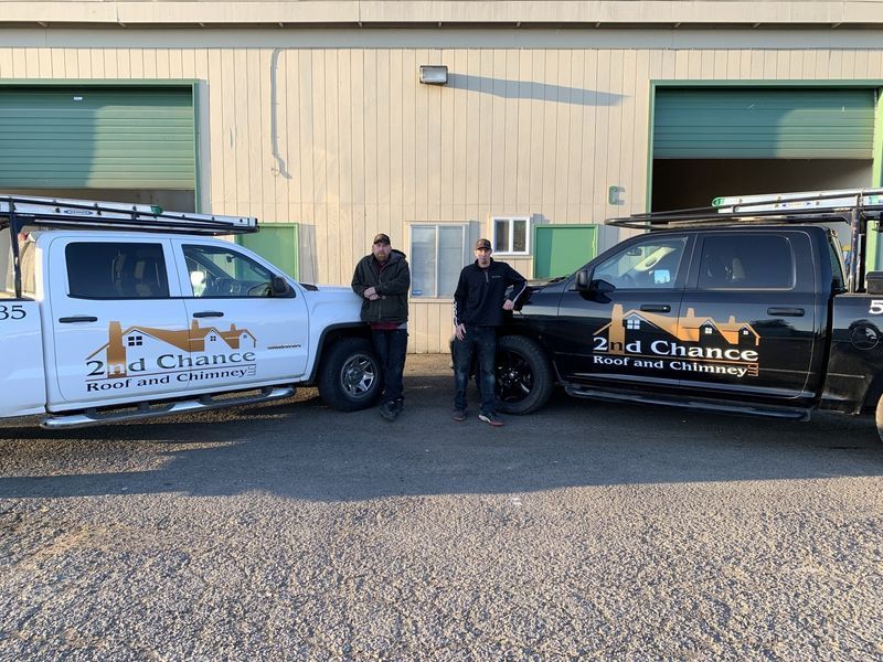 Two men standing between work trucks in front of a building. Trucks have company logo: 2nd Chance Roof and Chimney.