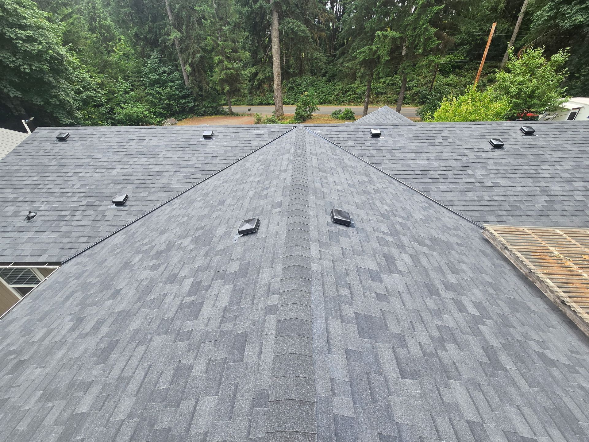 New gray shingle roof with vents, viewed from above, surrounded by trees