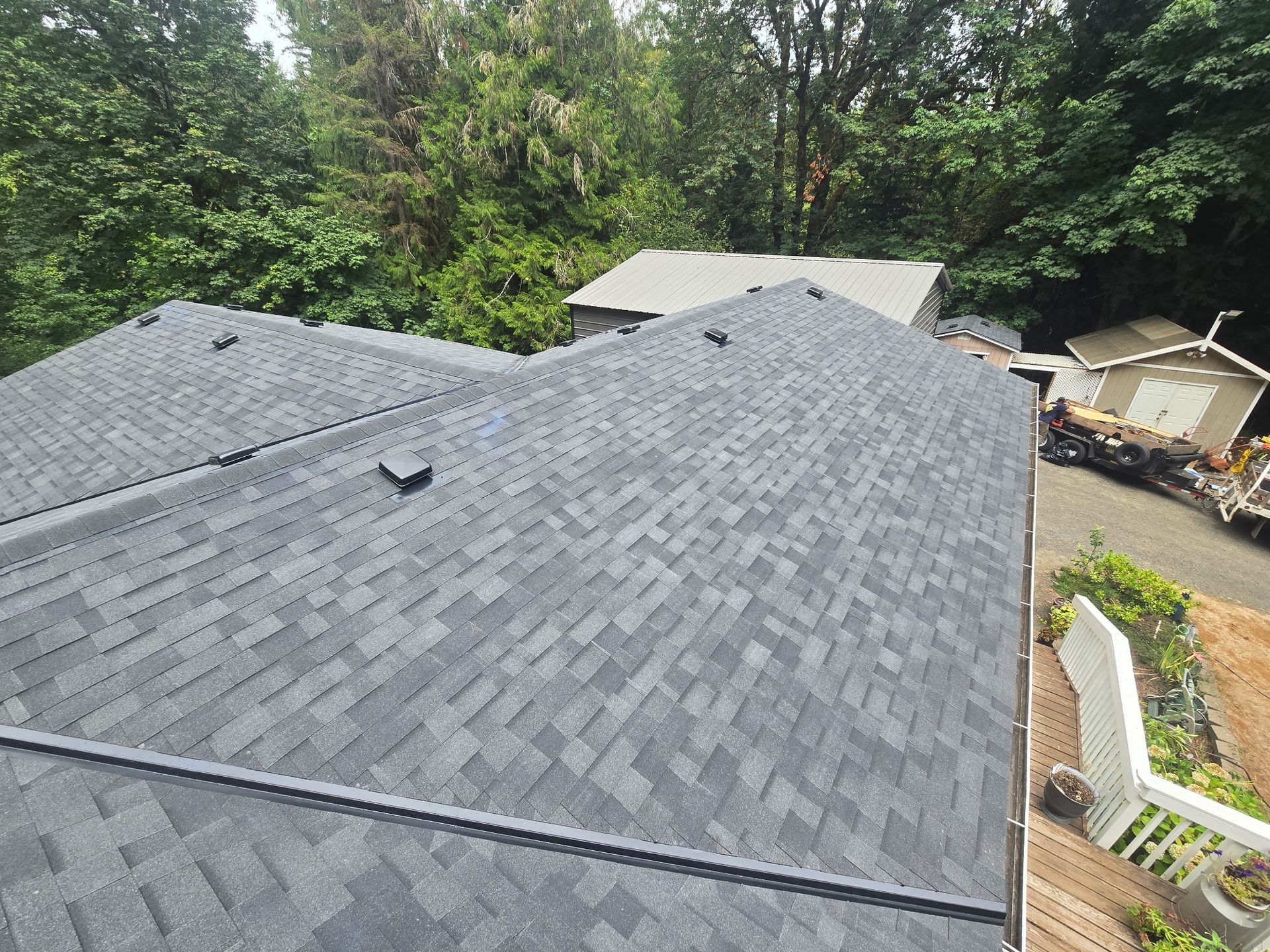 View over dark gray shingled rooftops with trees and a small yard below