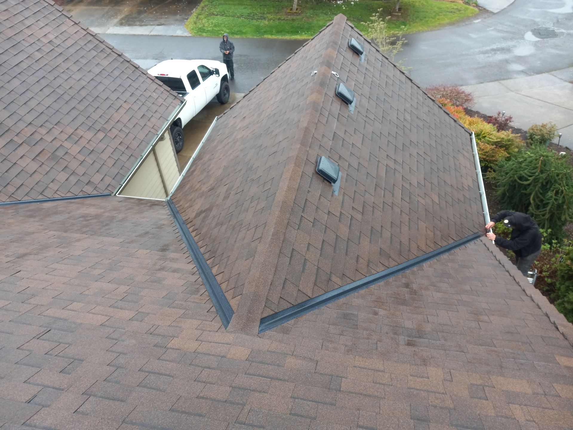 Aerial view of brown shingled rooftops with skylights and a parked white car near a driveway