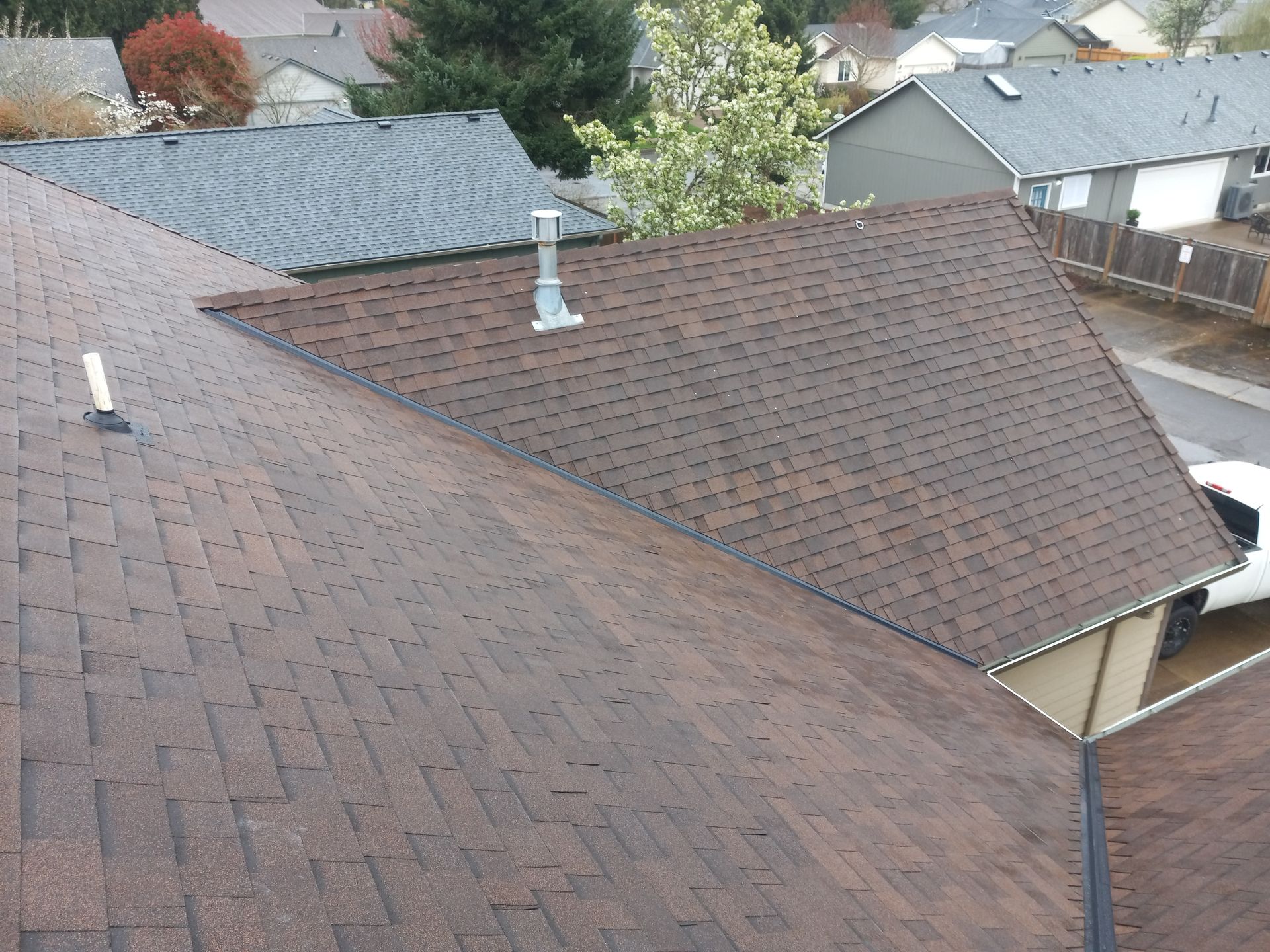 Rooftops of suburban houses with brown and gray shingles, seen from above.