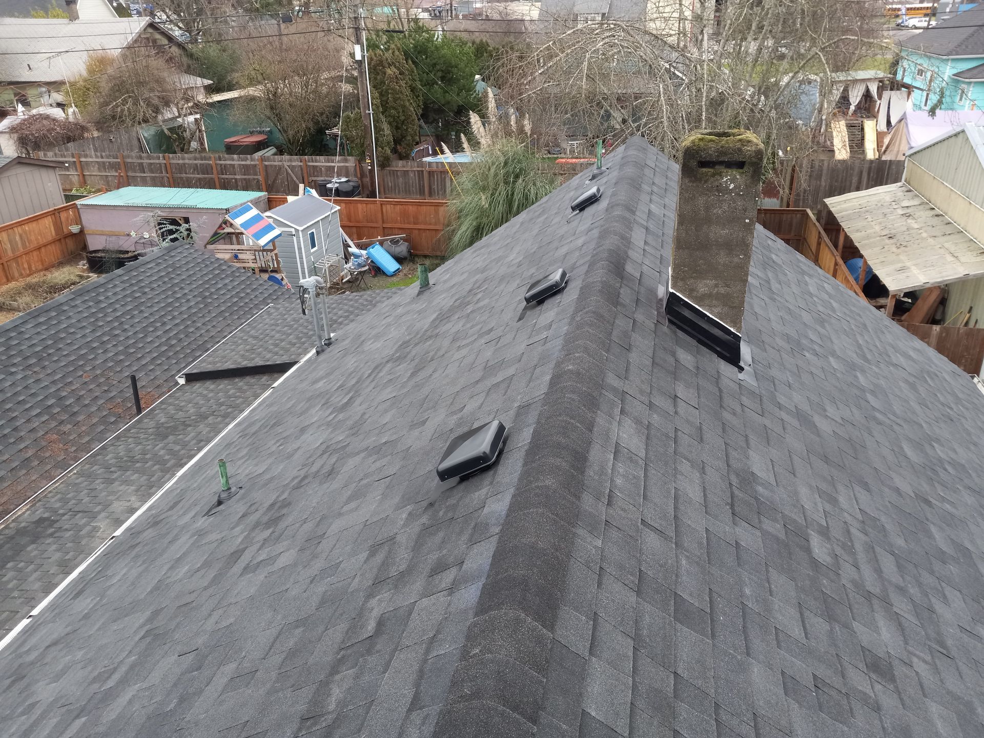 Aerial view of a gray shingled roof with vents in a residential neighborhood