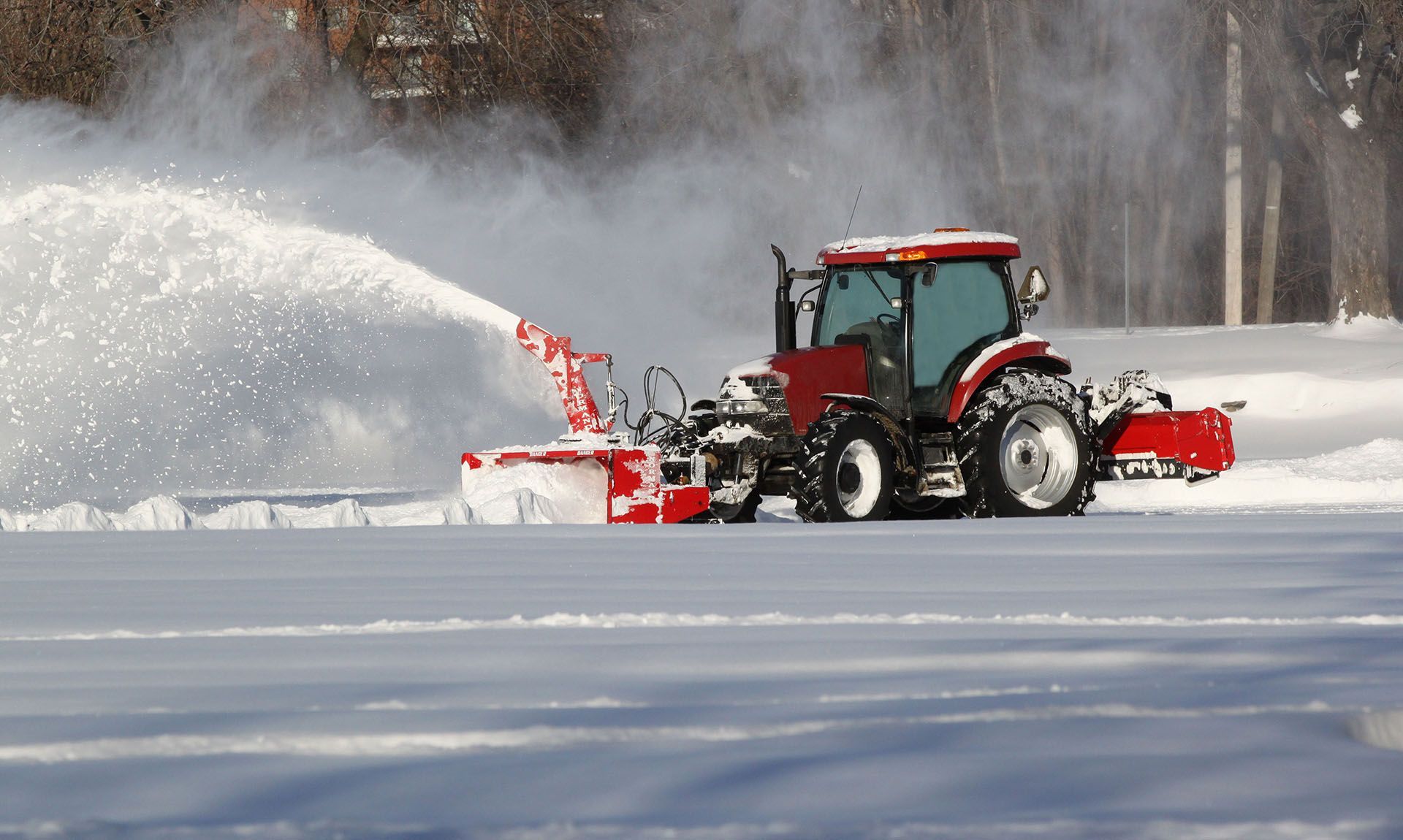 A red tractor is blowing snow on a snowy road.