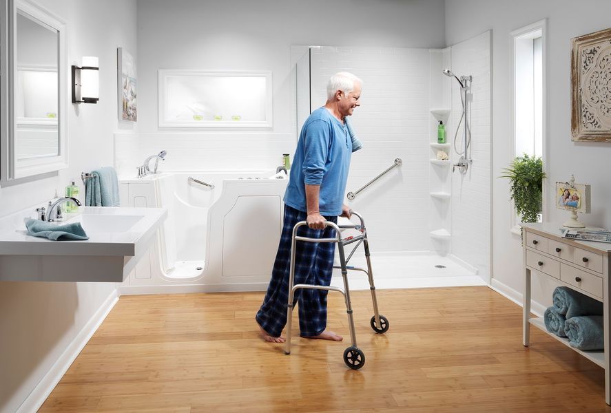 An older man using a walker in a remodeled bathroom with a walk-in tub and accessible shower.