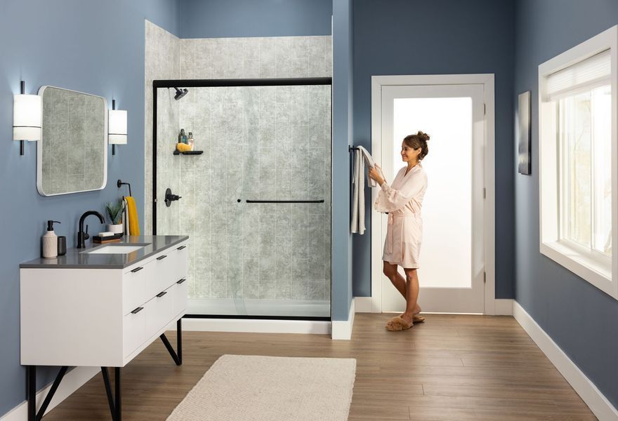 Bathroom with blue walls, woman in robe, vanity, shower with textured glass, and white trim.