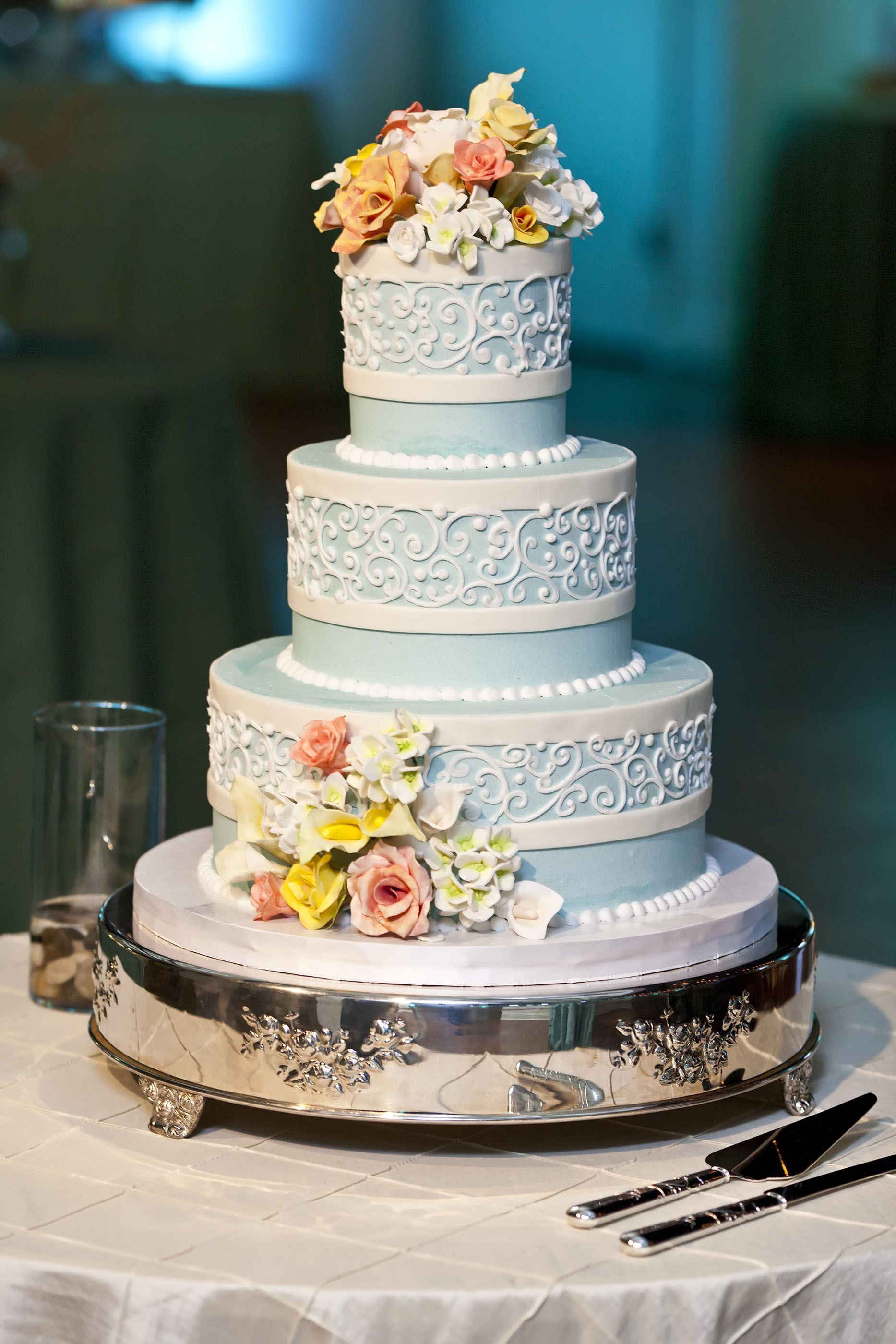 Three-tier white wedding cake with pastel flowers on a silver stand at a decorated table