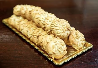 Two rows of almond-coated pastries on a gold tray on a wooden table