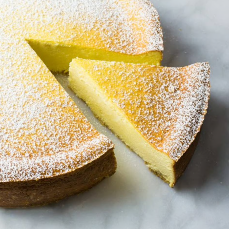 Powdered sugar-covered cake slice on a white plate, with one wedge cut out revealing a yellow interior