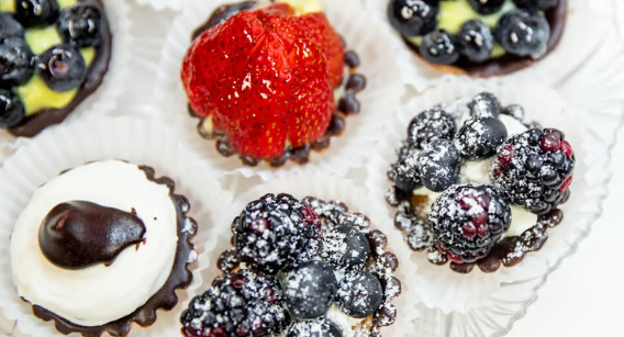 Assorted fruit tarts topped with berries and powdered sugar on a white tray