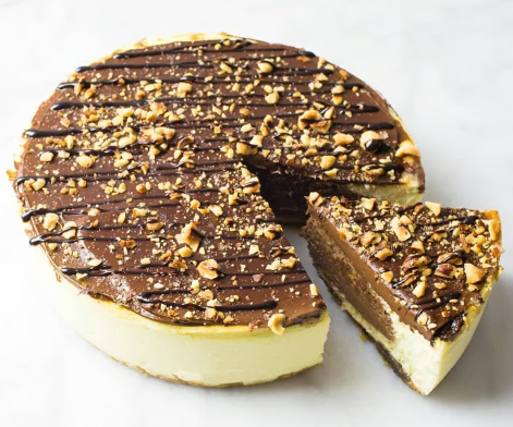 Chocolate and nut-topped cheesecake with a slice cut out on a white background