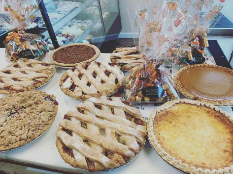 Assorted pies and a cake arranged on a table, with floral decor in the background.