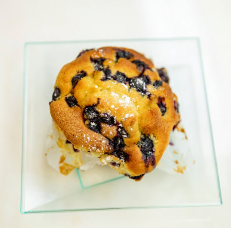 Blueberry muffin on a square glass plate with crumbs and powdered sugar.