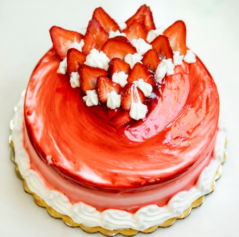 Red strawberry cake with glossy frosting and sliced strawberries on top, on a white platter.