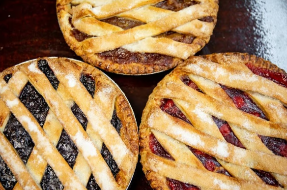 Three lattice-top fruit pies on a dark surface, with golden crusts and one showing red filling.