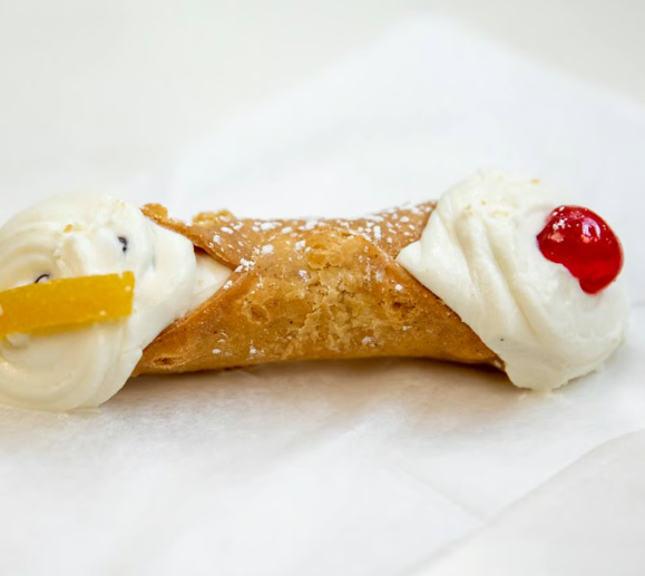 Cannoli pastry with white cream filling, a yellow fruit garnish, and a red cherry on a white plate