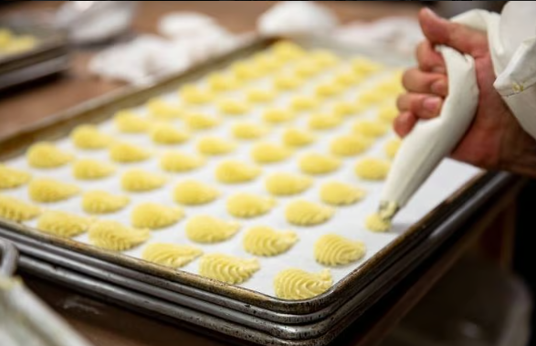 Piping dough onto trays of small yellow cookies in a bakery kitchen