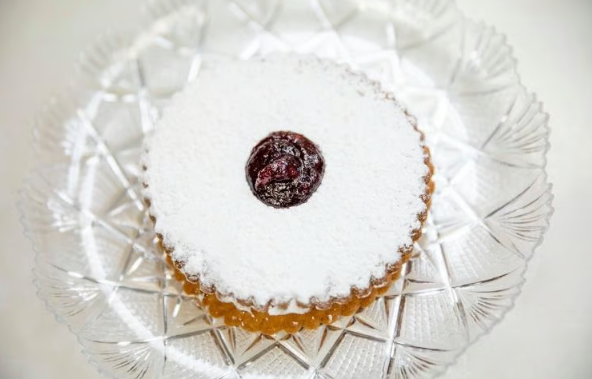 Powdered sugar-topped cake on a clear glass plate with a berry center