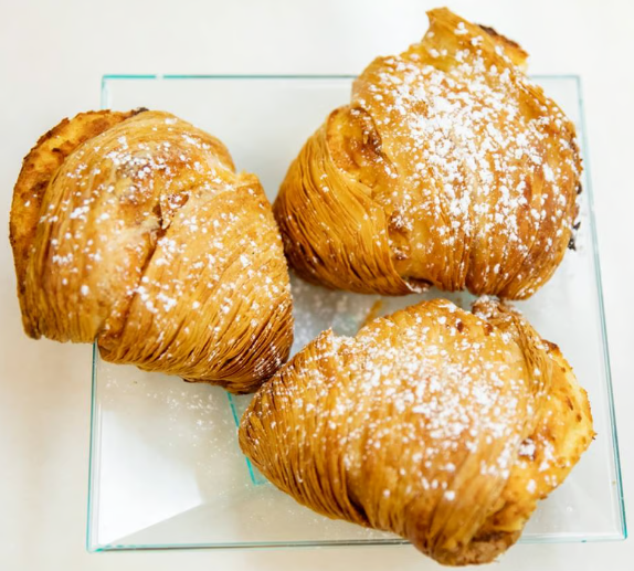 Three golden-brown croissants dusted with powdered sugar on a clear glass plate