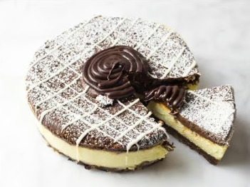 Chocolate layered cake with white drizzle, chocolate topping, and one slice cut out